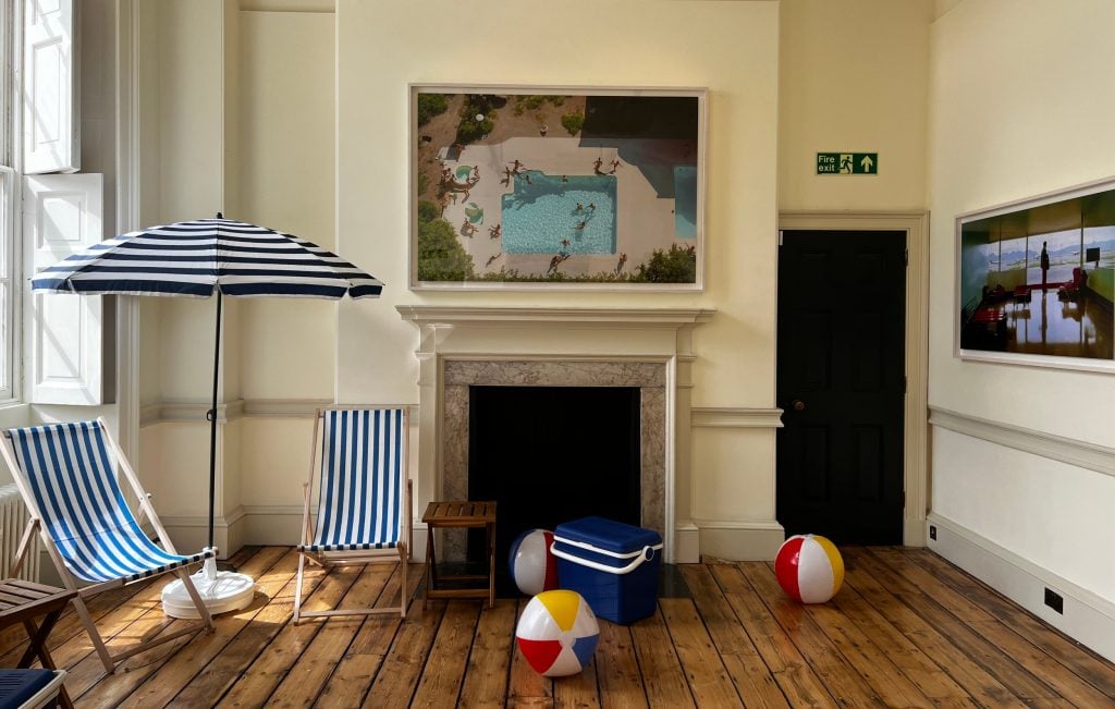 photograph of a large room with photos of holiday scenes on the wall and holiday items like a parasol and deck chairs and beach balls fill the space around the photos
