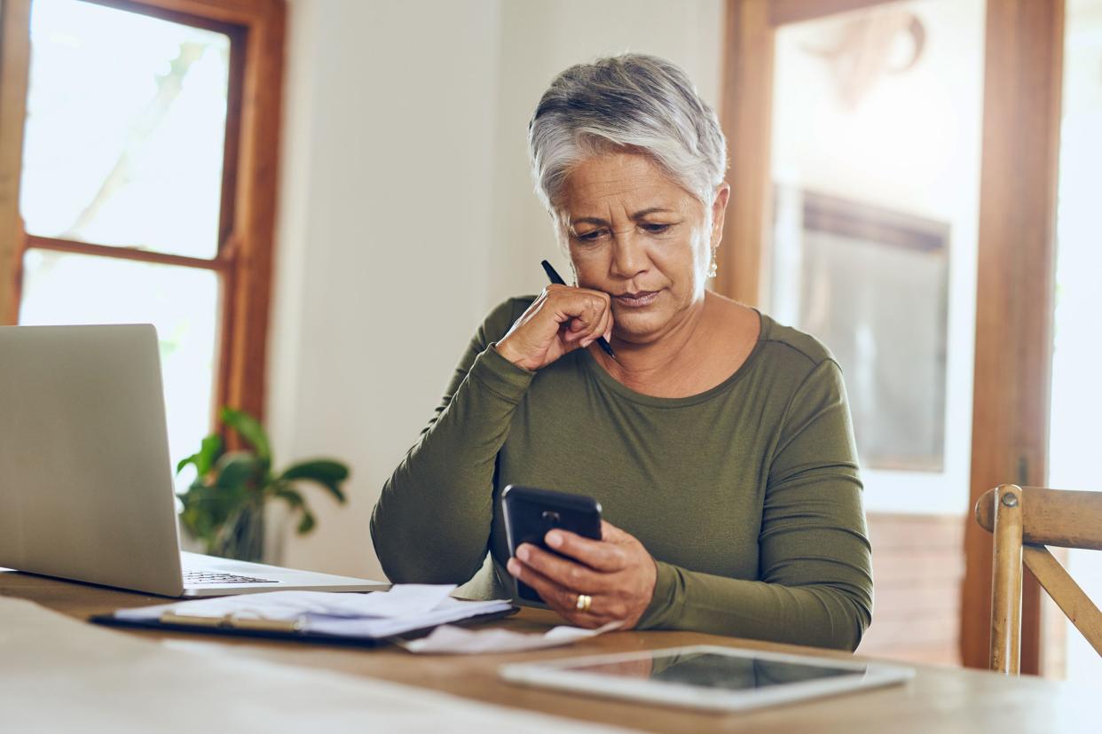 senior woman sitting at home with laptop and phone, investing
