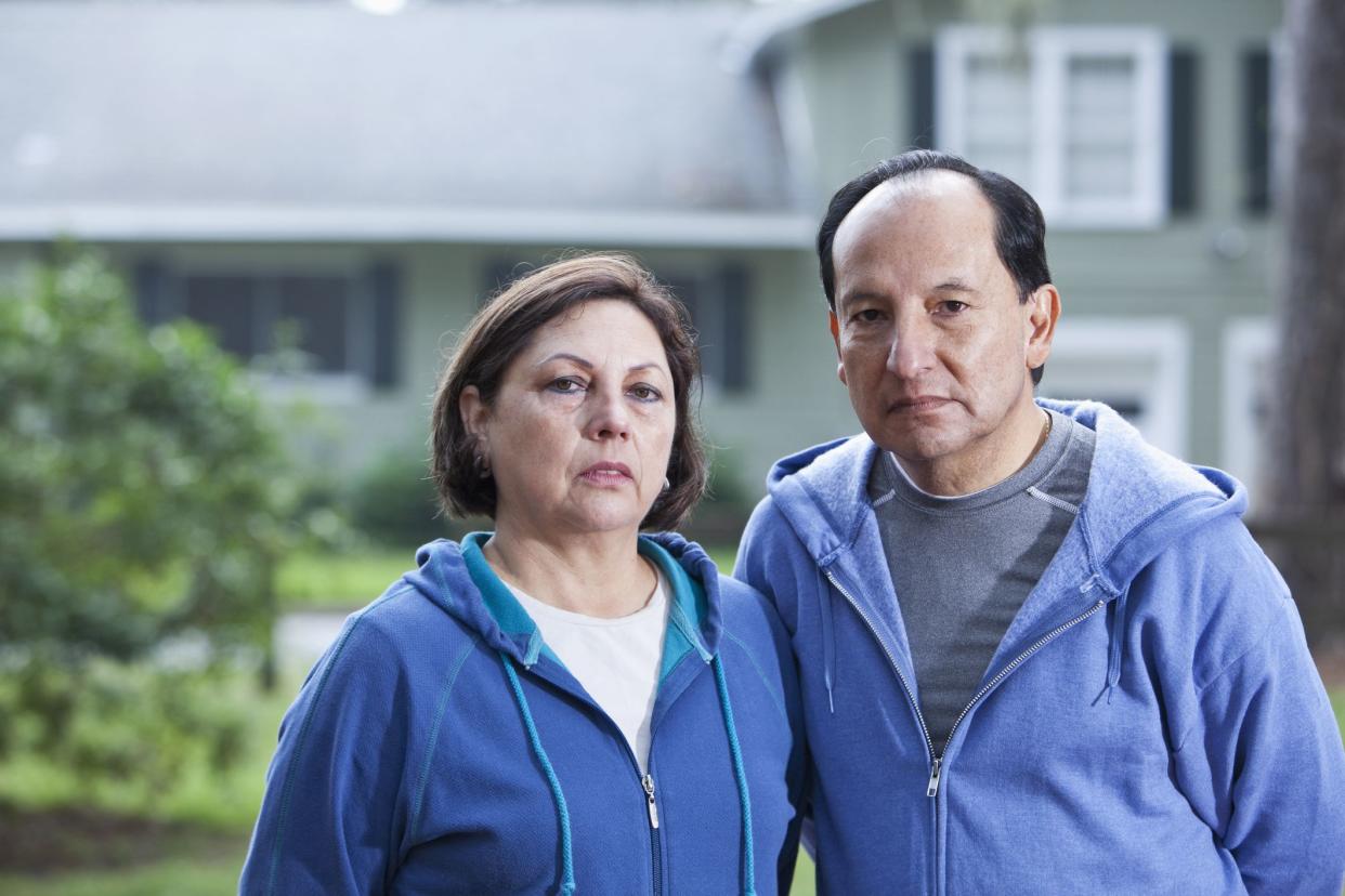 Portrait of serious senior Hispanic couple standing outside house.