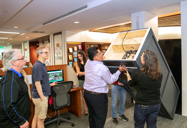 From left, Science Machine Shop Supervisor/Technician Jeff Britton, Senior Teaching Professor of Physics Evan Halstead, Zoë Bilodeau ’23, Omar Gomez ’23, and Associate Professor of Art Sarah Sweeney work together to install the phone booth in Scribner Library.