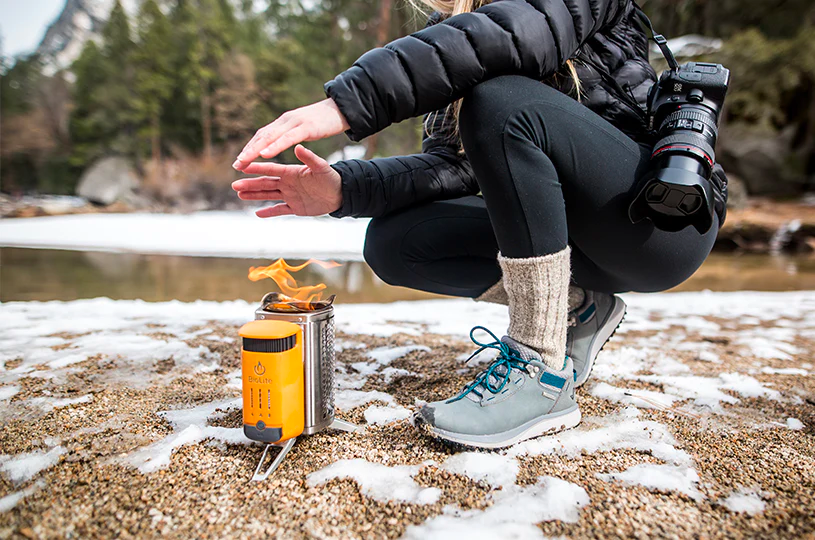A photographer takes a break from a winter hike to warm themselves using a BioLite stove.