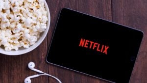 The Netflix (NFLX) logo on a tablet with earbuds and a bowl of popcorn nearby.