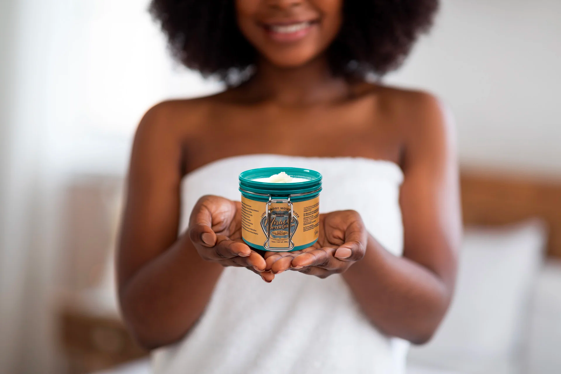 A person wearing a towel holds up a pot of body butter in this example of product photography.