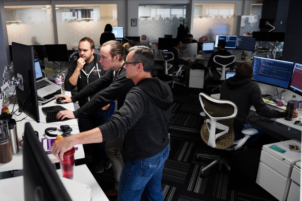 Platform engineer manager Rick Wager (left) and Devops engineer Alex Withrow (right) watching platform engineer Lucas Moore deploying test code to a staging instance for testing on day one for Denver's well-known startup's relaunch of their mobile app.