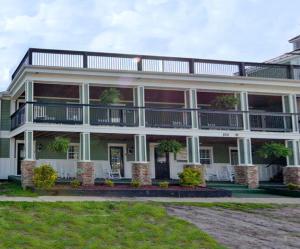 Front view of the Carolina Beach Inn showing a two-story building with a porch, balconies, and decorative plants. The building has a welcoming and cozy appearance.