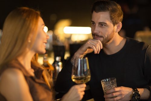 Bearded handsome man smiling thoughtfully listening to his beautiful woman talking while enjoying drinks together at the bar copyspace flirting dating romantic seduction couples communication