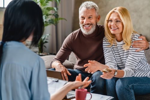 Personal financial adviser explaining terms of contract to happy middle aged couple on tablet.