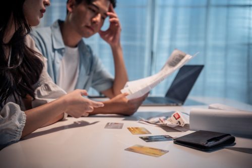 young depressed couple having argument while checking money debt. Attractive new marriage man and woman looking frustrated to paperwork and bill, feel worried about financial problem in house.