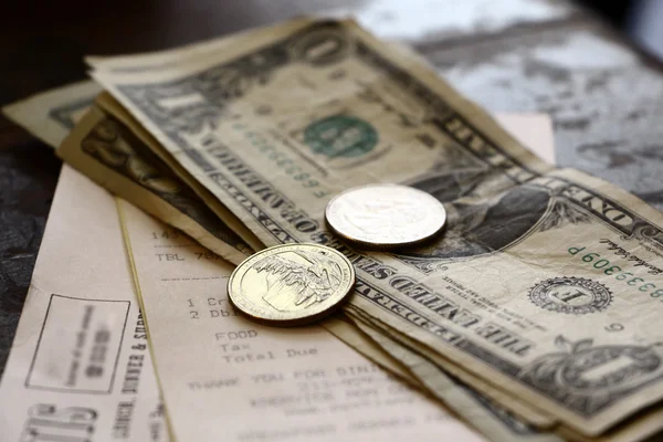 Close-up of paper currency, coins, and a receipt on a wooden surface.