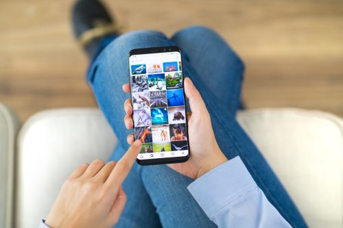 woman using smart phone on a couch. The smart phone is an iPhone 8 displaying Instagram application. iPhone is a touchscreen smartphone developed by Apple Inc.