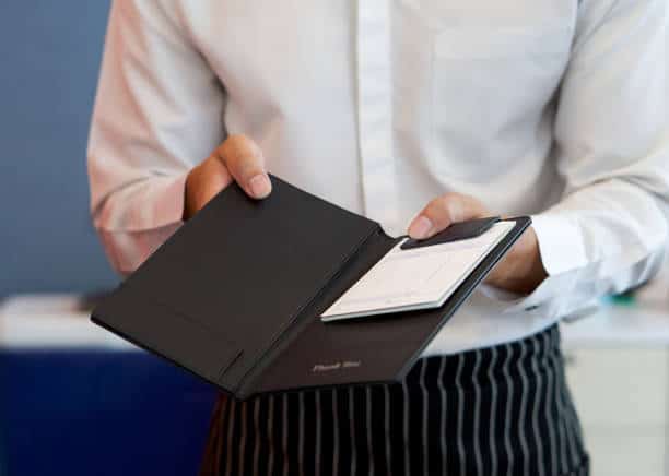 Waiter in a white shirt holding an open black bill holder with a receipt inside.