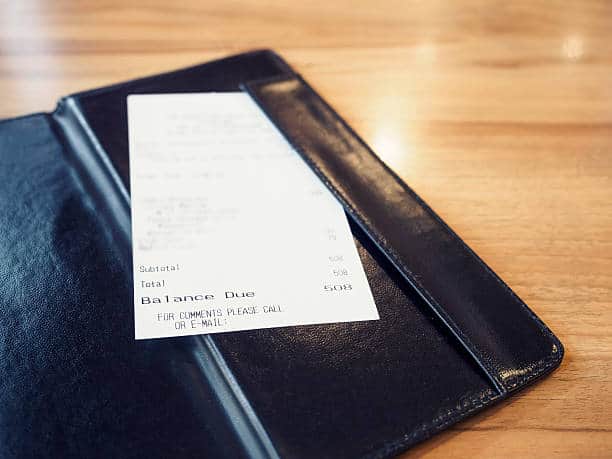 A receipt with a total of $508 is placed in a black check presenter on a wooden table.