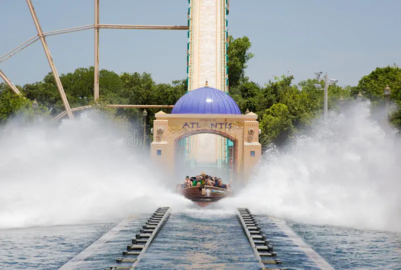 People on a water ride splash down a steep track, creating a large spray of water, with 