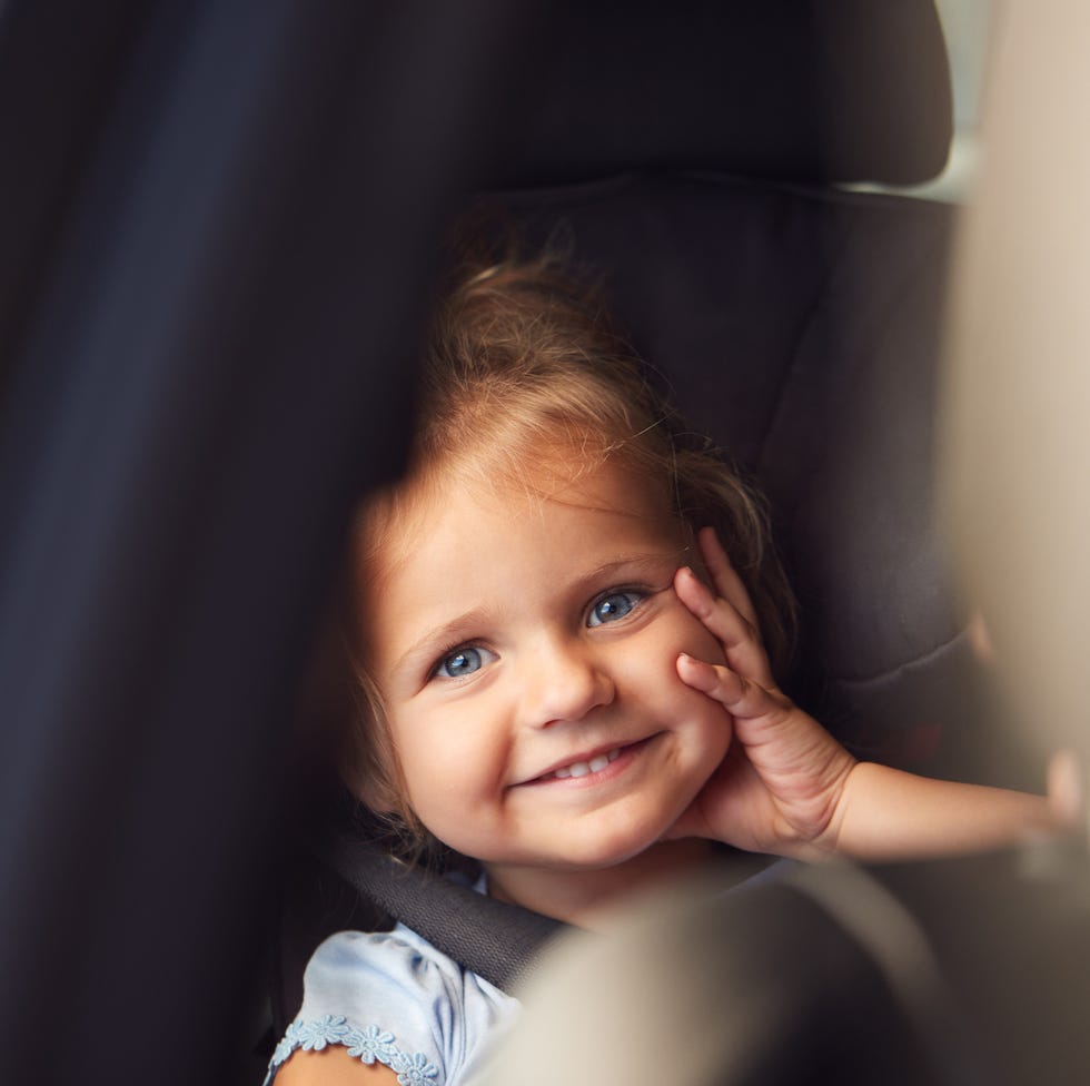 portrait of young girl sitting in child safety seat on car journey looking out of window