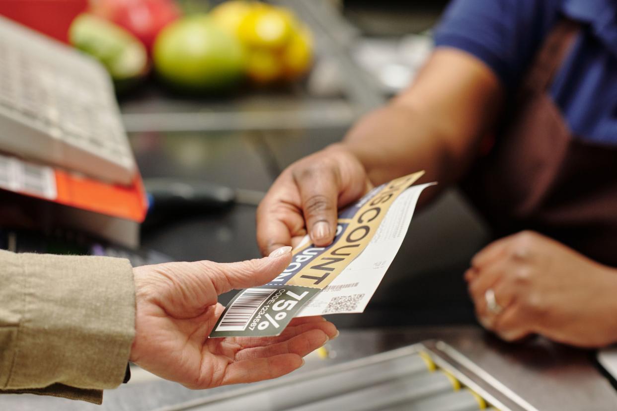 Hand of young African American female cashier passing discount coupon and receit to customer over checkout counter in supermarket