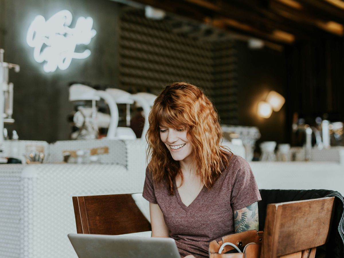 woman sitting on brown wooden chair while using silver laptop computer in room