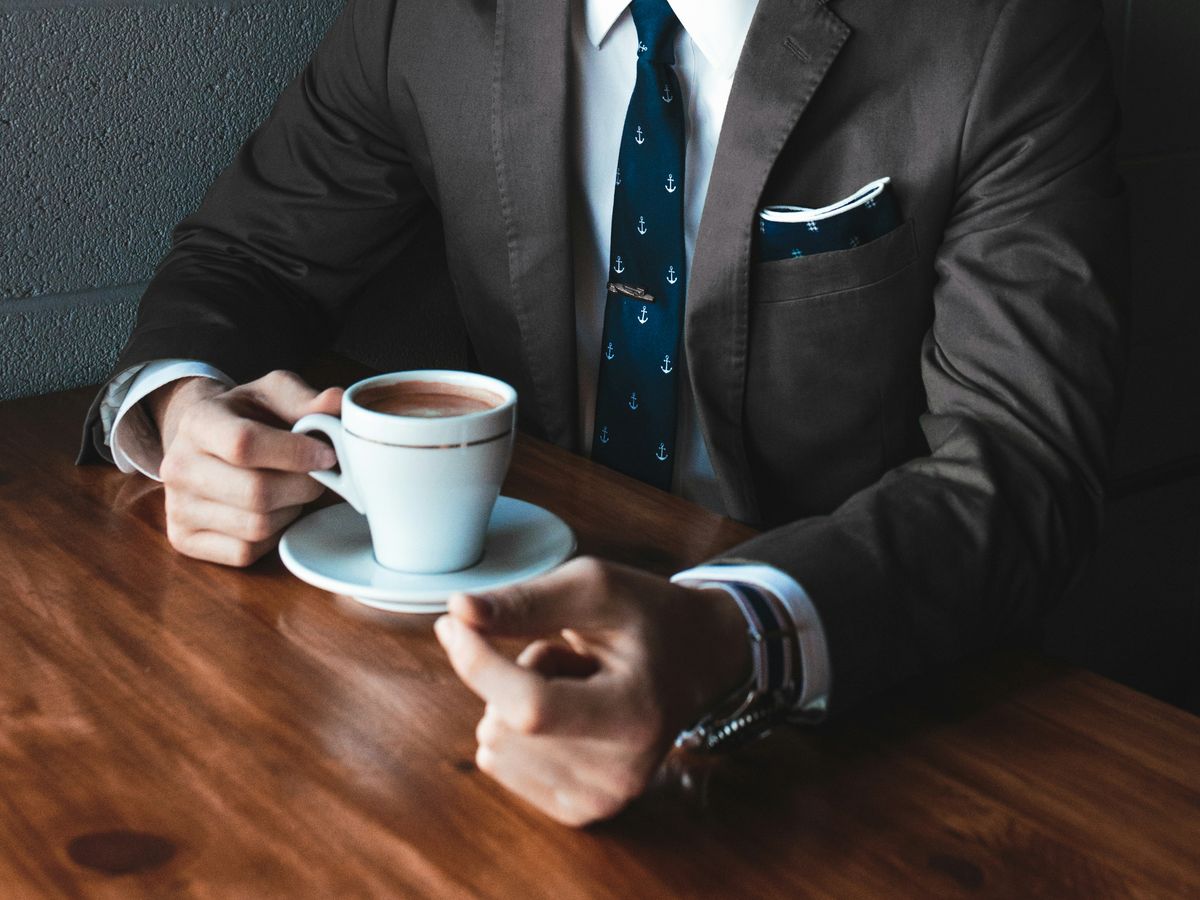 man holding cup filled with coffee on table