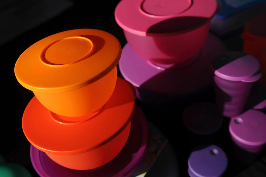 An image of orange, pink and purple round Tupperware boxes in a dark space.