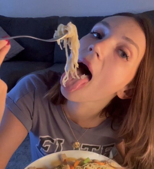 Gracie putting noodles in her mouth with a fork, hovering over a bowl of noodles