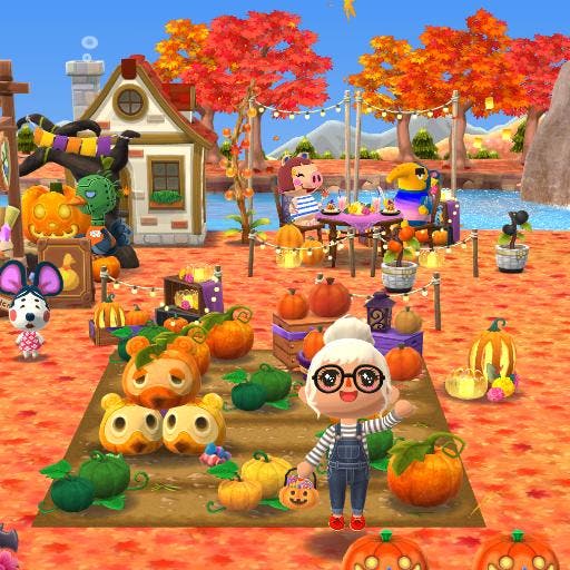 Screenshot of Animal Crossing Pocket Camp campsite layout with an autumn pumpkin theme. The player character is waving while holding a trick or treat pail, and two animals are having dinner as a cafe table in the background.