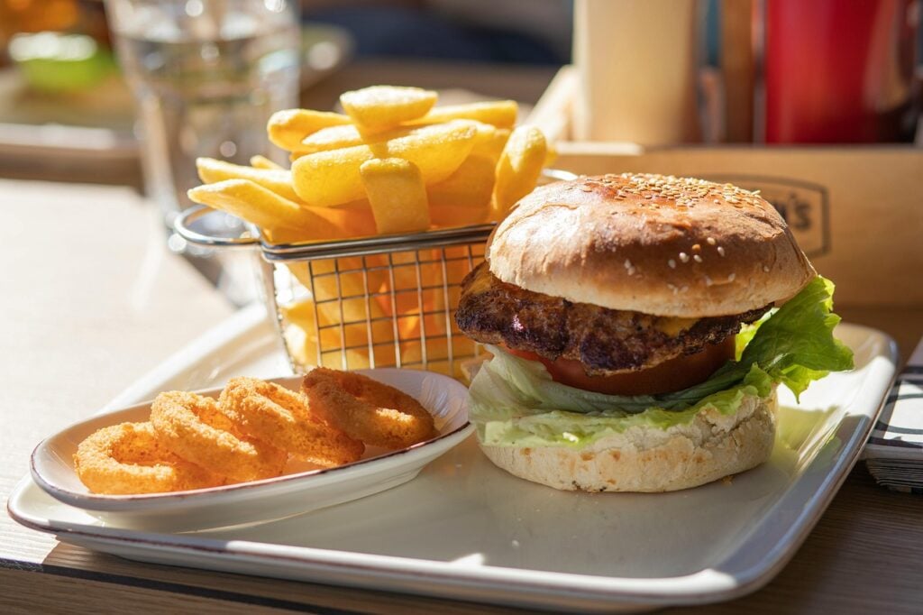 A plate with a burger topped with lettuce and tomato, accompanied by a side of curly fries and a small basket of regular fries.