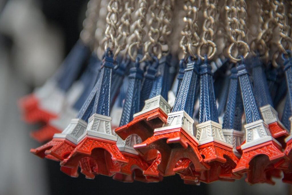 Close-up of numerous Eiffel Tower keychains, colored in blue, white, and red, hanging from metal chains.