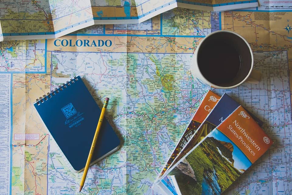 A Colorado map spread on a table with brochures, a notebook, a pencil, and a cup of coffee.