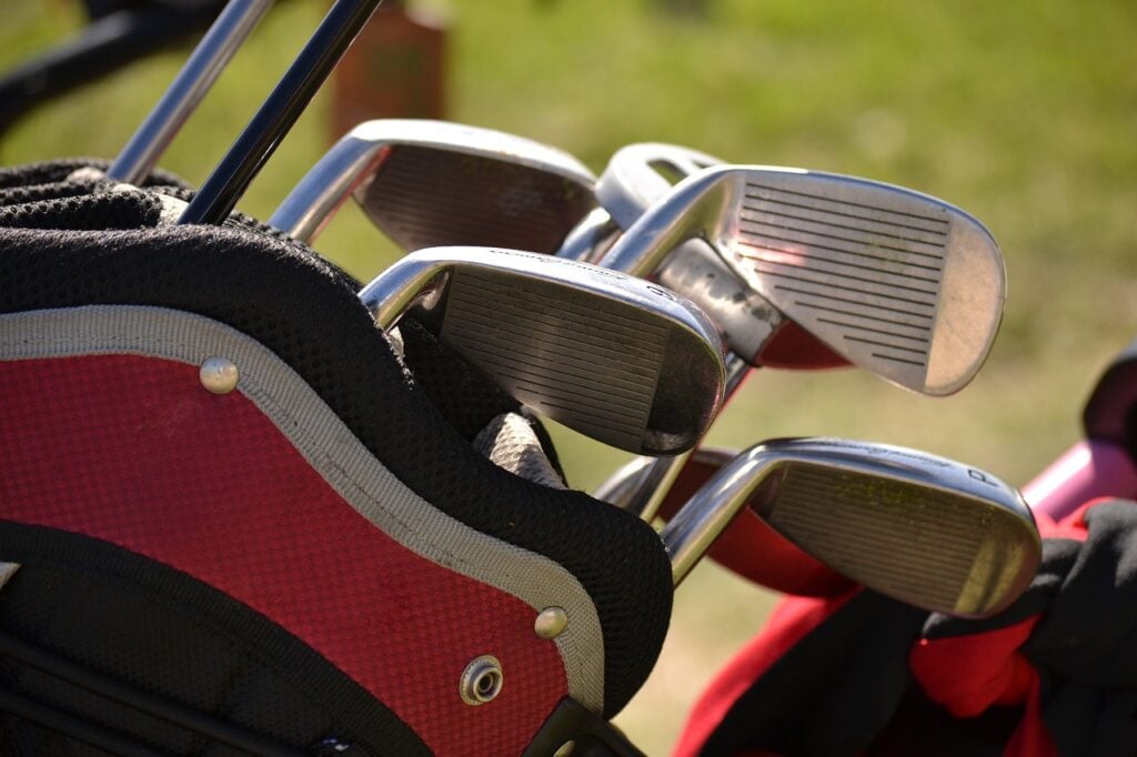 Close-up of a set of golf clubs in a red and black golf bag, with a grassy background.