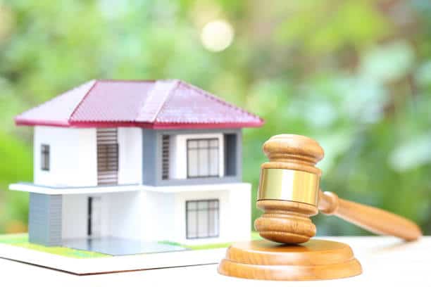 A small house model in the background with a wooden gavel in the foreground, symbolizing real estate law or property auction.