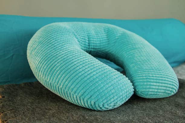 A blue, textured U-shaped neck pillow is resting on a gray surface with a blue background.