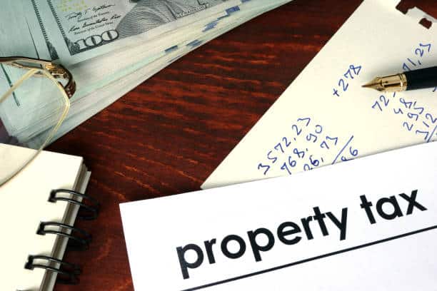 A stack of hundred-dollar bills next to a notepad, eyeglasses, pen, and a document labeled 