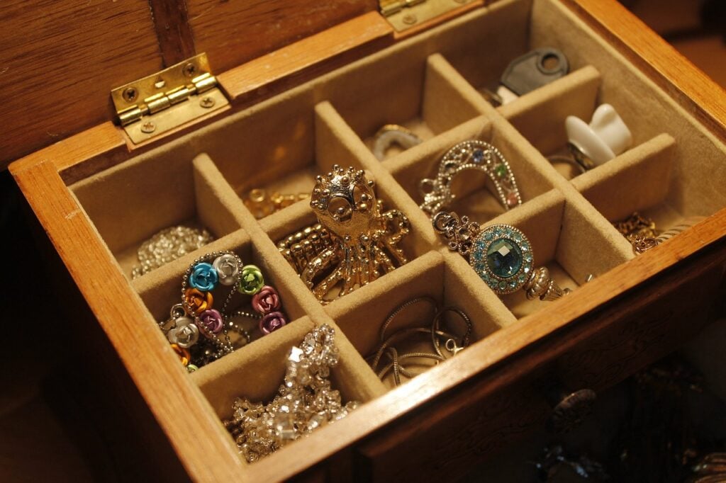 A wooden jewelry box with multiple compartments holds various pieces of jewelry, including rings, earrings, and bracelets.