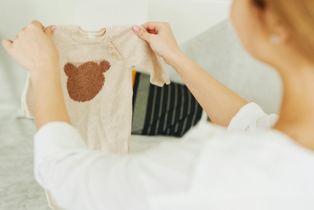 Woman holding a beige baby sweater with a knitted bear design.