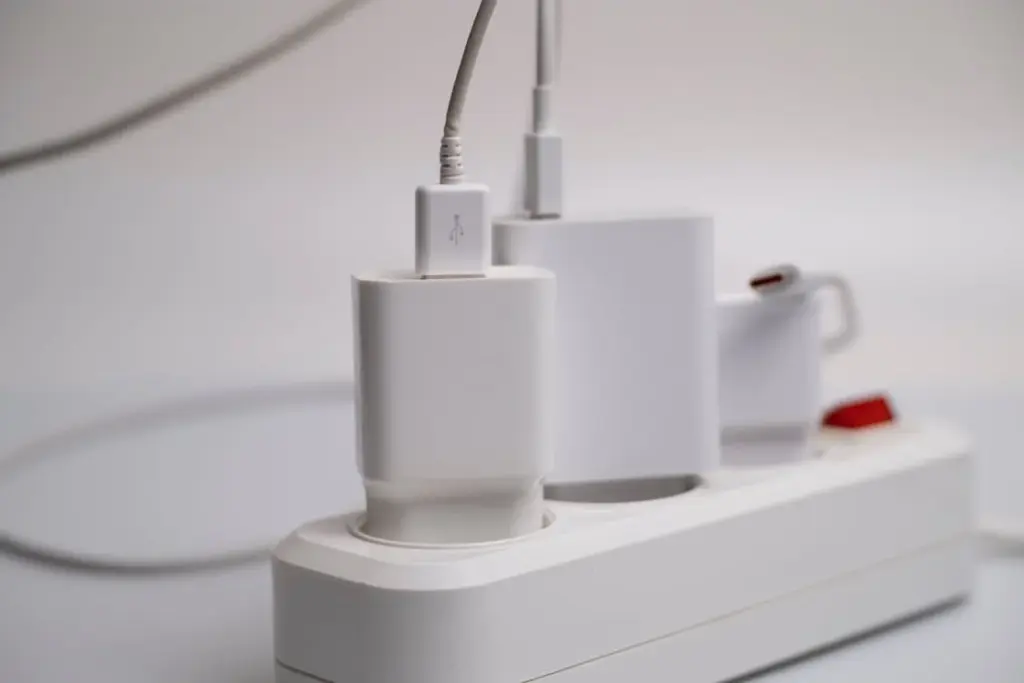 Close-up of a power strip with multiple electronic devices plugged in, including a USB charger and two charging adapters.