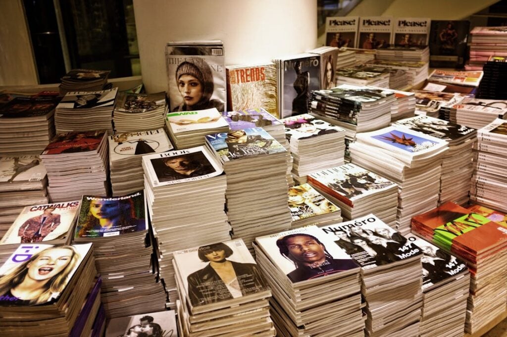 Stacks of various magazines are arranged on a table in a store, displaying a wide range of topics and covers.