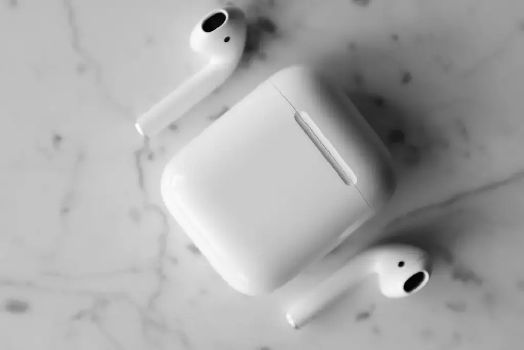 A pair of white wireless earbuds with an open charging case on a marble surface.