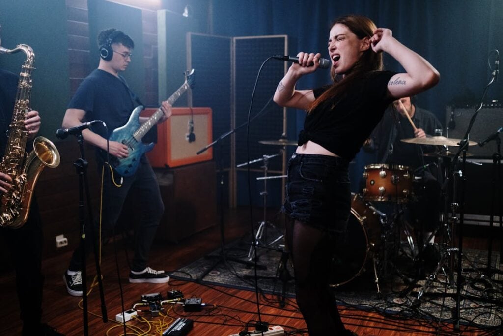 Band performing in a dimly lit studio, with a singer passionately singing into a microphone, a guitarist, a saxophonist, and a drummer playing their instruments.