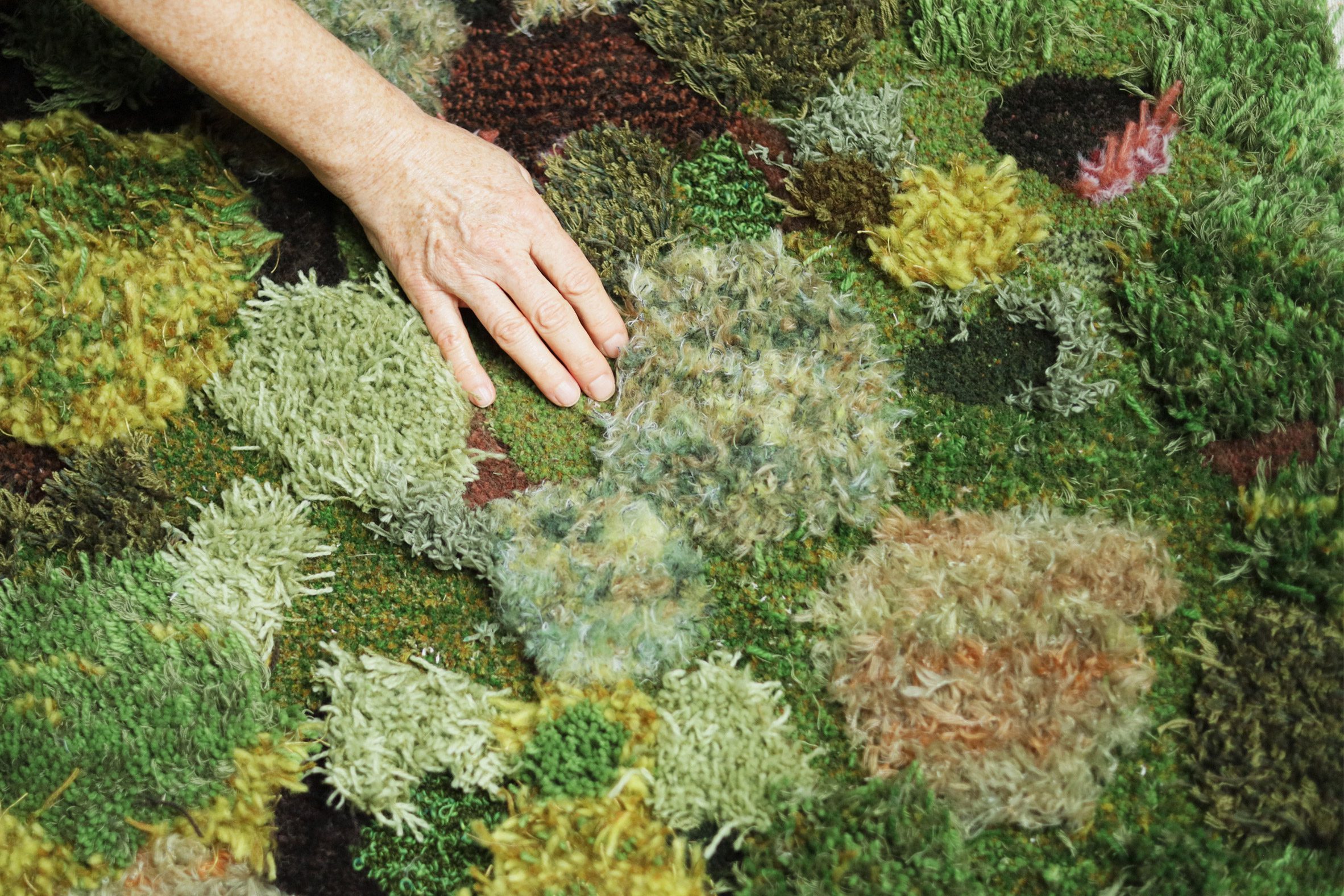 A photograph of a person's hand interacting with a multi-textured surface in colours of green, yellow and orange.