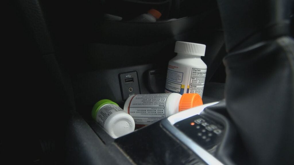 Several medication bottles are scattered in a car's center console near a USB port and gear shift.