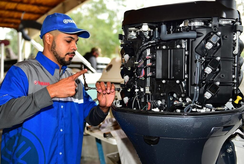 Mechanic in a blue uniform repairs an engine, using a tool and checking connections in a workshop setting.