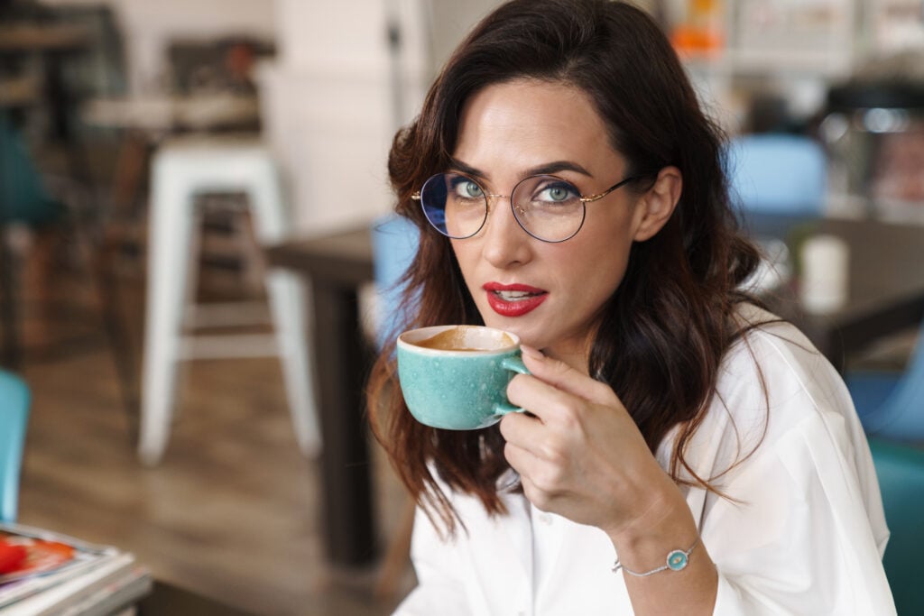 Person with glasses holding a blue mug, seated at a table in a café setting.