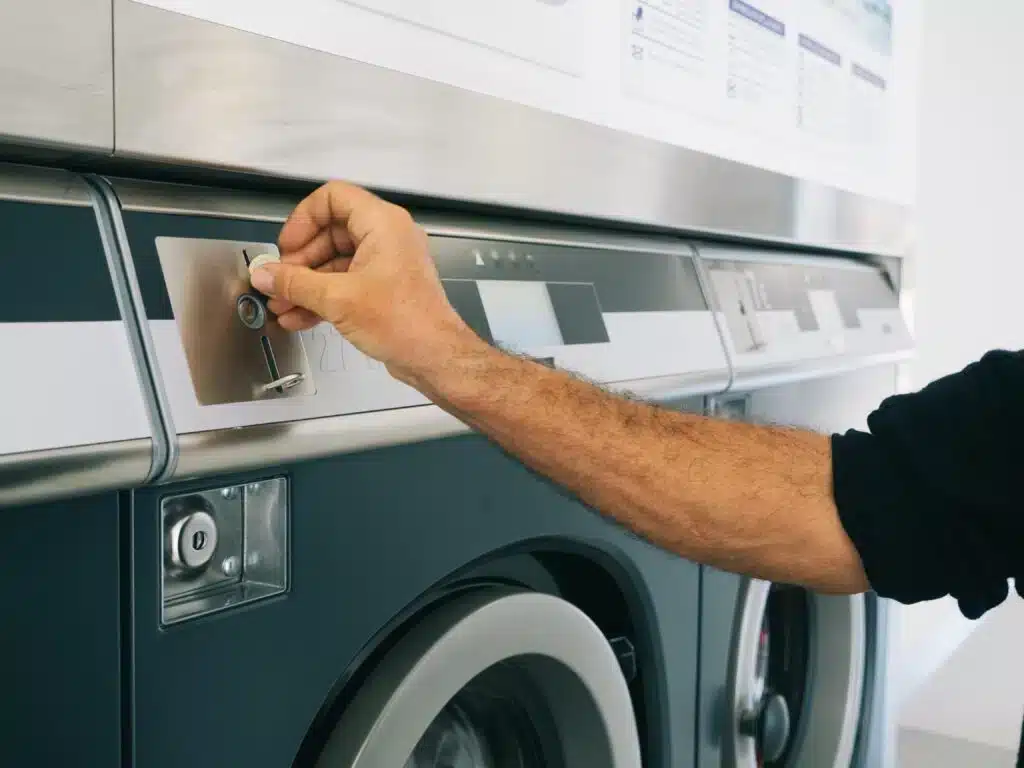 A person inserting a coin into a laundromat washing machine.