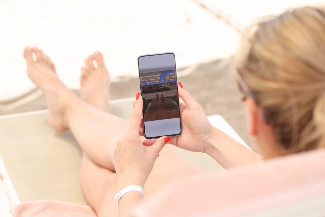 Young woman lying on sun lounger on beach and taking pictures of her feet on mobile phone closeup