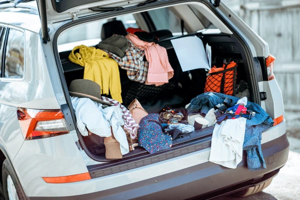 Open car trunk filled with disorganized clothes, bags, and miscellaneous items.