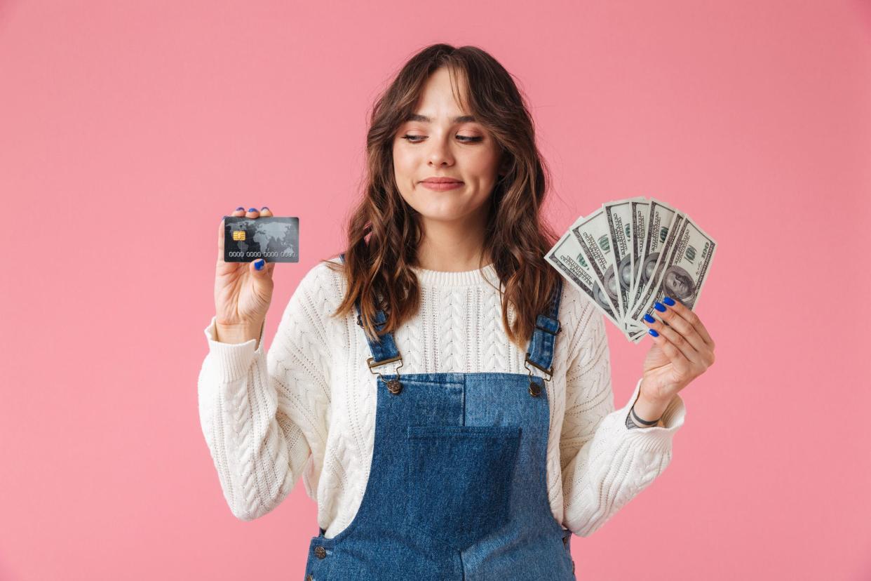 Portrait of a confident young girl holding money banknotes and showing credit card isolated over pink background