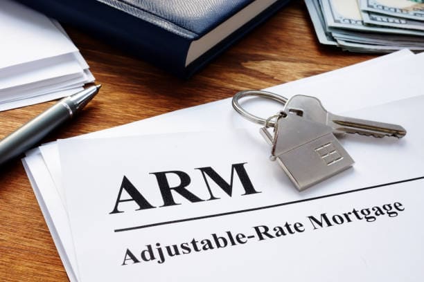 Adjustable-Rate Mortgage (ARM) document with house key and pen on a desk, alongside a stack of papers and a stack of cash in the background.