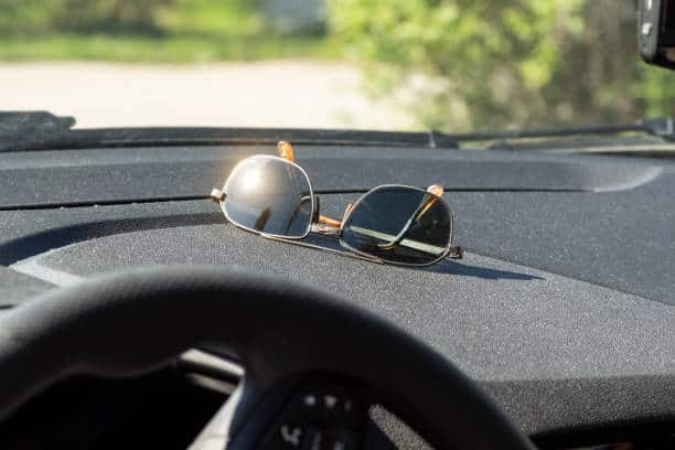 Sunglasses resting on a car dashboard, with sunlight reflecting off the lenses.