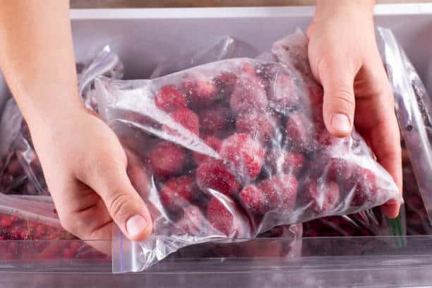 Hands holding a sealed plastic bag filled with frozen strawberries.