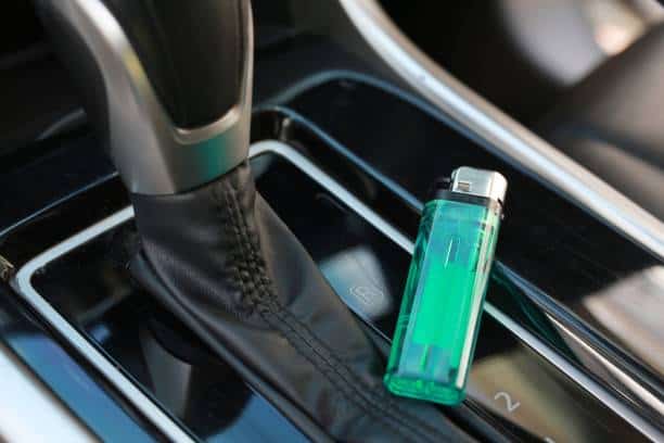 A green lighter is placed on the center console of a car, next to the gear shift.