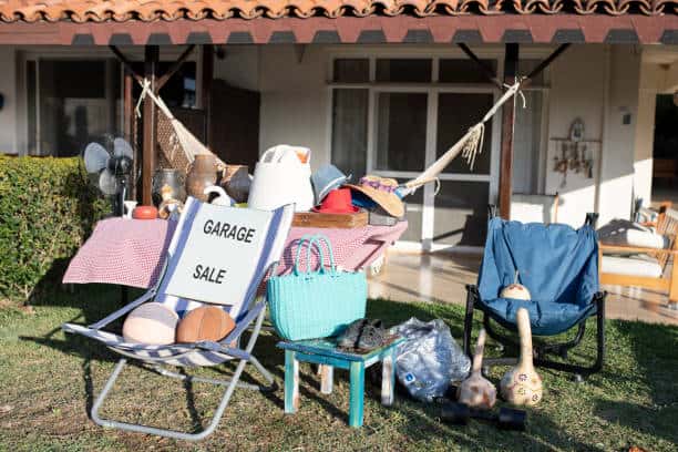 A garage sale setup with various items on display, including chairs, bags, and household items, with a 